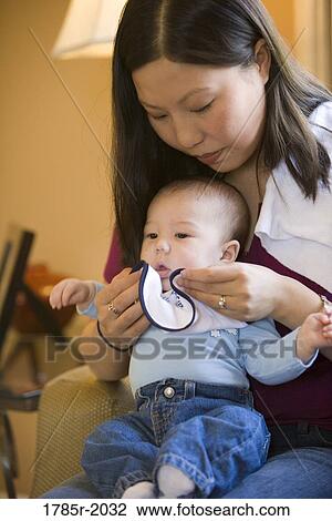 Mother holding infant boy on her lap while wiping his face with a bib View Large Photo Image Stock Image - Mother holding infant boy on her lap while wiping his face with a bib. Fotosearch