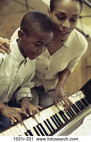 Stock Image - Mother teaching her son to play the piano. Fotosearch