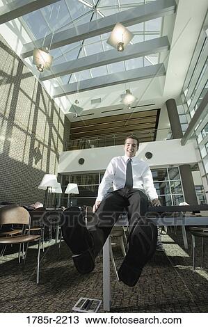 Stock Image - Office worker sitting on table. Fotosearch