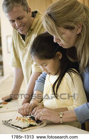 Stock Image - Parents and adopted Asian daughter making sushi. Fotosearch