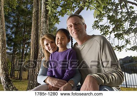 Stock Image - Parents sitting with daughter in backyard. Fotosearch