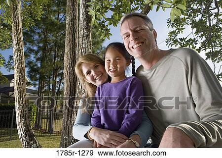 Stock Photo - Parents sitting with daughter in backyard. Fotosearch