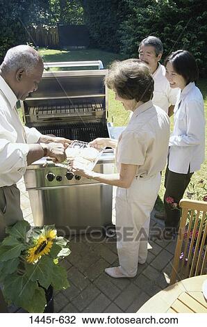 Stock Image - People standing around a barbecue grill. Fotosearch
