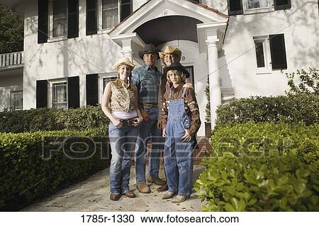 Stock Image - Portrait of a family in country clothes standing in front of a house. Fotosearch