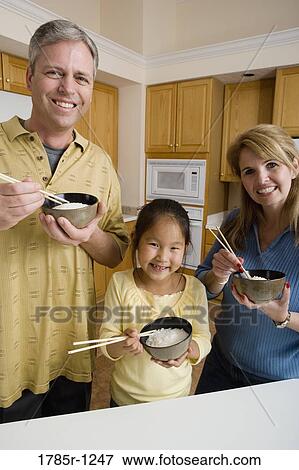 Portrait of a family in kitchen holding bowls of rice and chopsticks View Large Photo Image Stock Photo - Portrait of a family in kitchen holding bowls of rice and chopsticks. Fotosearch