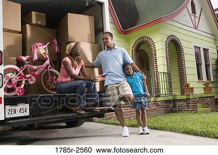 Stock Image - Portrait of a family standing outside a house by moving truck. Fotosearch