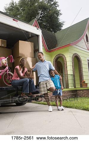 Stock Image - Portrait of a family standing outside a house by moving truck. Fotosearch