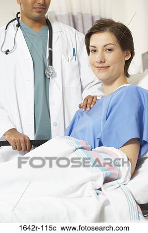 Stock Image - Portrait of a female patient smiling with a male doctor standing beside her. Fotosearch