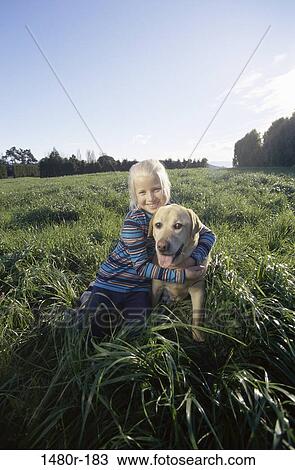 Stock Image - Portrait of a girl hugging her dog sitting on grass. Fotosearch