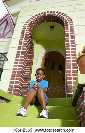 Stock Image - Portrait of a girl sitting on front steps of house. Fotosearch