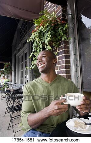 Stock Image - Portrait of a laughing young man holding a coffee cup at a sidewalk cafÄ. Fotosearch