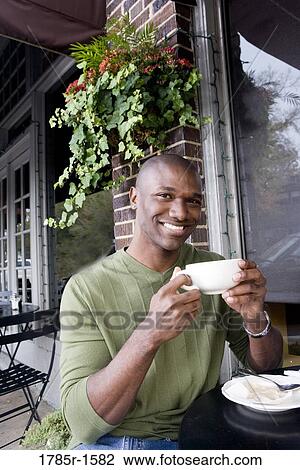 Stock Image - Portrait of a laughing young man holding a coffee cup at a sidewalk cafÄ. Fotosearch
