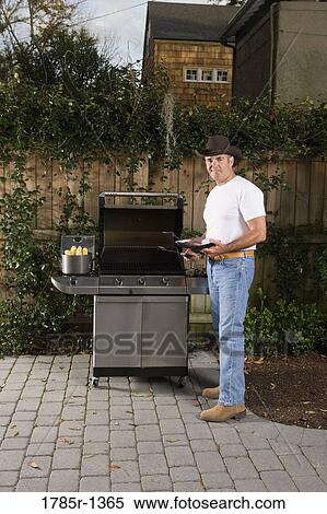 Stock Photography - Portrait of a mature man standing near barbeque grill. Fotosearch