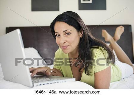 Stock Image - Portrait of a mature woman lying in the bed and using a laptop. Fotosearch