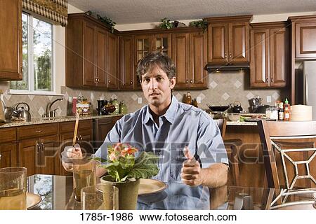 Stock Photograph - Portrait of a mid adult man sitting at dining table waiting to be served. Fotosearch