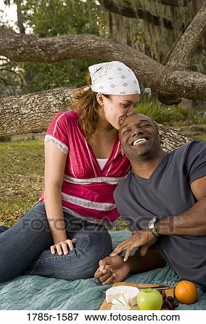 Stock Photo - Portrait of a romantic young couple lying on a picnic blanket under oak trees. Fotosearch