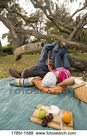 Stock Photo - Portrait of a romantic young couple lying on a picnic blanket under oak trees. Fotosearch