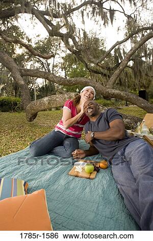 Portrait of a romantic young couple lying on a picnic blanket under oak trees View Large Photo Image Stock Photograph - Portrait of a romantic young couple lying on a picnic blanket under oak trees. Fotosearch