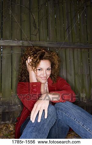 Portrait of a smiling young woman with hands running through her hair, sitting against a wooden fence View Large Photo Image Stock Photograph - Portrait of a smiling young woman with hands running through her hair, sitting against a wooden fence. Fotosearch