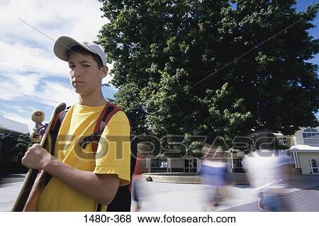 Portrait of a teenage boy standing outdoors holding a skateboard View Large Photo Image Stock Photo - Portrait of a teenage boy standing outdoors holding a skateboard. Fotosearch