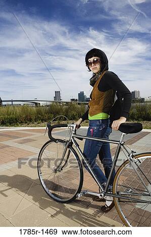 Stock Photo - Portrait of a young Asian woman standing with her bicycle. Fotosearch