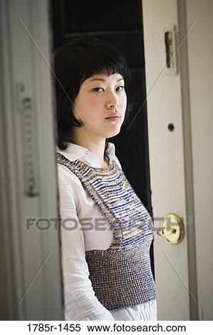 Stock Photography - Portrait of a young Asian woman standing at front door. Fotosearch