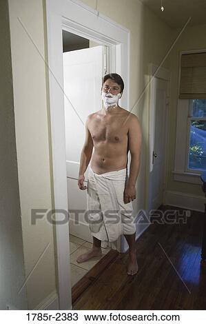 Stock Image - Portrait of a young man shaving wearing a towel. Fotosearch