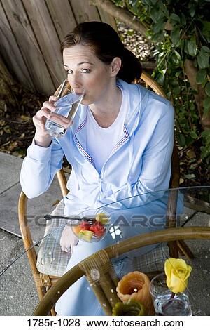 Stock Photo - Portrait of a young woman drinking a glass of water on patio. Fotosearch