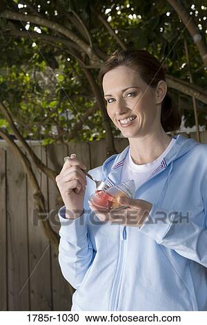 Portrait of a young woman eating fresh fruit from a bowl in backyard View Large Photo Image Stock Image - Portrait of a young woman eating fresh fruit from a bowl in backyard. Fotosearch