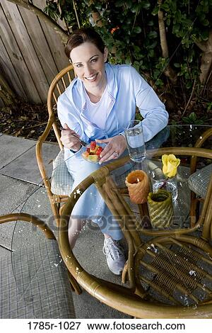 Portrait of a young woman eating fresh fruit on patio View Large Photo Image Stock Photo - Portrait of a young woman eating fresh fruit on patio. Fotosearch