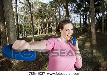 Portrait of a young woman exercising with hand weights in a park View Large Photo Image Stock Photo - Portrait of a young woman exercising with hand weights in a park. Fotosearch