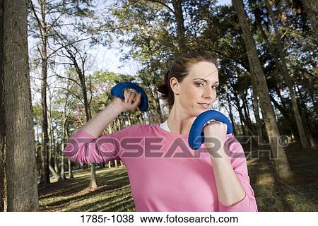 Portrait of a young woman exercising with hand weights in a park View Large Photo Image Stock Photo - Portrait of a young woman exercising with hand weights in a park. Fotosearch