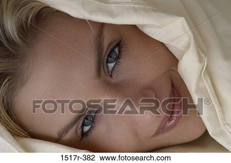 Stock Image - Portrait of a young woman lying in bed smiling. Fotosearch