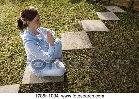 Portrait of a young woman sitting on a stepping stone in a yoga position View Large Photo Image Picture - Portrait of a young woman sitting on a stepping stone in a yoga position. Fotosearch