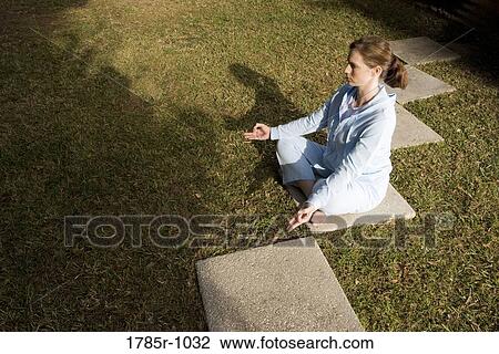 Stock Image - Portrait of a young woman sitting on a stepping stone in a yoga position. Fotosearch