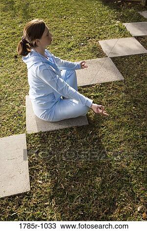Portrait of a young woman sitting on a stepping stone in a yoga position View Large Photo Image Stock Image - Portrait of a young woman sitting on a stepping stone in a yoga position. Fotosearch