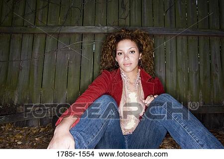 Portrait of a young woman sitting against a wooden fence View Large Photo Image Picture - Portrait of a young woman sitting against a wooden fence. Fotosearch