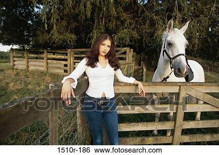 Stock Photograph - Portrait of a young woman standing against a wooden fence. Fotosearch