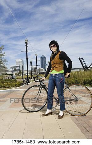 Stock Image - Portrait of a young woman standing with her bicycle. Fotosearch