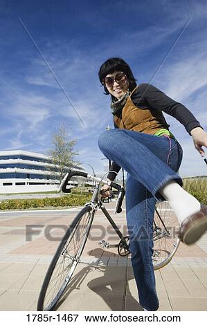 Portrait of a young woman standing with her bicycle, kicking View Large Photo Image Stock Photo - Portrait of a young woman standing with her bicycle, kicking. Fotosearch