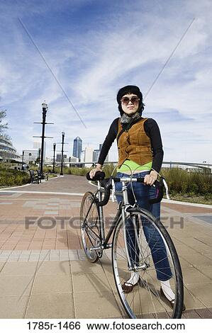 Stock Photograph - Portrait of a young woman standing with her bicycle. Fotosearch
