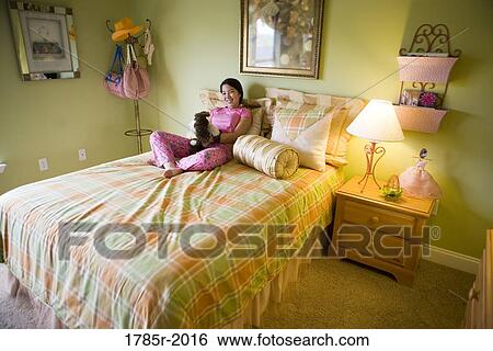 Stock Photograph - Portrait of an Asian-Caucasian teenage girl in pajamas sitting on her bed. Fotosearch