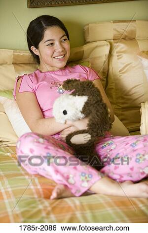 Portrait of an Asian-Caucasian teenage girl in pajamas sitting on her bed holding stuffed animal View Large Photo Image Stock Photograph - Portrait of an Asian-Caucasian teenage girl in pajamas sitting on her bed holding stuffed animal. Fotosearch