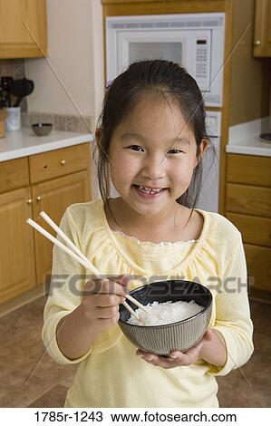Portrait of an Asian girl in kitchen holding bowl of rice and chopsticks View Large Photo Image Stock Image - Portrait of an Asian girl in kitchen holding bowl of rice and chopsticks. Fotosearch