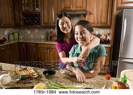 Portrait of an Asian mother embracing her Asian-Caucasian daughter in the kitchen View Large Photo Image Picture - Portrait of an Asian mother embracing her Asian-Caucasian daughter in the kitchen. Fotosearch