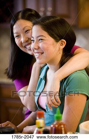 Stock Photo - Portrait of an Asian mother embracing her Asian-Caucasian daughter in the kitchen. Fotosearch