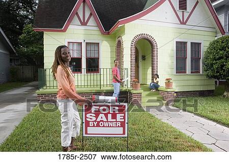 Stock Photo - Portrait of family outside house with woman standing by "For Sale" sign. Fotosearch