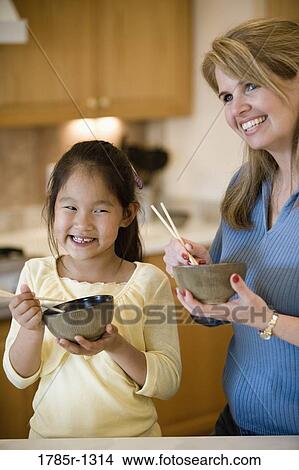 Portrait of mother and daughter in kitchen holding bowls of rice and chopsticks View Large Photo Image Picture - Portrait of mother and daughter in kitchen holding bowls of rice and chopsticks. Fotosearch