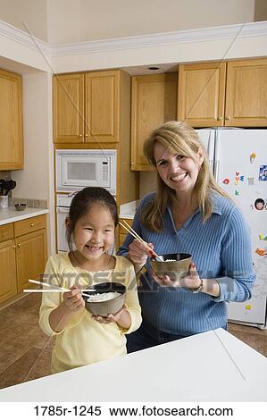 Portrait of mother and daughter in kitchen holding bowls of rice and chopsticks View Large Photo Image Stock Photography - Portrait of mother and daughter in kitchen holding bowls of rice and chopsticks. Fotosearch