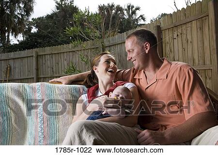 Portrait of smiling parents with baby sitting in backyard View Large Photo Image Stock Image - Portrait of smiling parents with baby sitting in backyard. Fotosearch